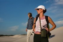 Пара с рюкзаком, стоящим на песке в солнечный день — стоковое фото