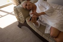 Donna disabile che utilizza il telefono cellulare sul divano di casa . — Foto stock