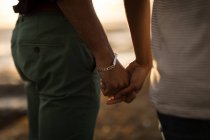 Mittelteil eines romantischen Paares, das sich bei Sonnenuntergang an einem Strand an der Hand hält — Stockfoto