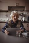 Пожилая женщина пользуется цифровым планшетом на кухне дома — стоковое фото