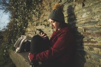 Жінка використовує мобільний телефон проти кам'яної стіни на відкритому повітрі . — стокове фото