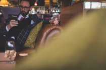 Uomo d'affari che utilizza il telefono cellulare pur avendo whisky nel bar — Foto stock