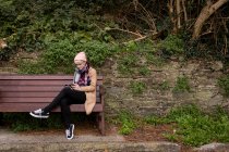 Frau sitzt auf Bank und benutzt Handy im Park — Stockfoto