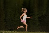 Menina bonito correr perto da margem do rio em um dia ensolarado — Fotografia de Stock