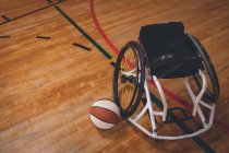 Пустое инвалидное кресло и баскетбольный мяч на корте — стоковое фото