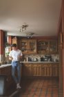 Mann benutzt Handy und hält Tasse Kaffee in Küche zu Hause. — Stockfoto