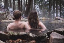 Rear view of couple relaxing in hot spring during winter — Stock Photo