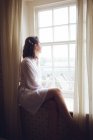 Задумчивая женщина смотрит в окно дома — стоковое фото