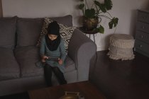 Muslim girl sitting on sofa and using digital tablet at home — Stock Photo