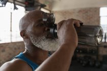 Nahaufnahme eines älteren Mannes, der Wasser im Fitnessstudio trinkt. — Stockfoto