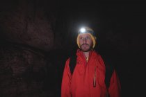 Турист, стоящий в темной пещере с фонариком на голове и рюкзаком — стоковое фото