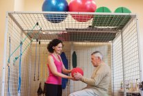 Женщина-терапевт помогает мужчине старшего возраста с мячом для упражнений в доме престарелых — стоковое фото