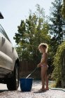 Chica llenando agua en cubo mientras se lava el coche - foto de stock