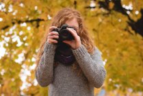 Donna che scatta una foto con fotocamera digitale nel parco autunnale — Foto stock
