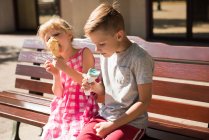 Hermano comiendo helado en el banco durante el día soleado - foto de stock