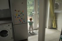 Взгляд сзади на маленькую девочку, выглядывающую через дверь дома — стоковое фото
