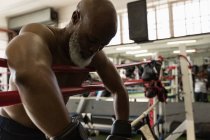 Senior boxer leaning on boxing ring in fitness studio. — Stock Photo