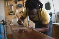 Carpenter painting wooden plank in workshop — Stock Photo