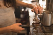 Barista usando uma adulteração para pressionar café moído em um portafilter no café — Fotografia de Stock
