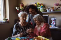 Две пожилые женщины делают искусственный цветок со смотрителем в доме престарелых — стоковое фото