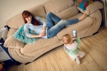 Малышка с матерью смотрит на мобильный телефон дома — стоковое фото