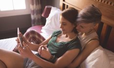 Пару лесбіянок обіймати і використовуючи цифровий планшетний в спальні в домашніх умовах. — стокове фото
