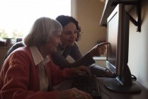 Смотритель помогает пожилой женщине во время работы за компьютером в сестринской комнате — стоковое фото