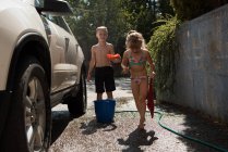 Irmãos lavando um carro na garagem exterior em um dia ensolarado — Fotografia de Stock