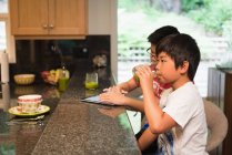 Frères et sœurs utilisant une tablette numérique dans la cuisine à la maison — Photo de stock