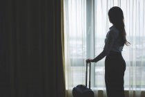 Geschäftsfrau blickt durch Fenster in Hotelzimmer — Stockfoto