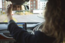 Исполнительница регулирует зеркало заднего вида во время вождения автомобиля — стоковое фото