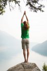 Fit man performing stretching exercise on the edge of a rock at the time of dawn — Stock Photo