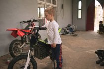 Little kid standing with bike in garage — Stock Photo