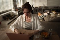Junge Frau benutzt ihren Laptop neben dem Essen auf dem Tisch im heimischen Wohnzimmer — Stockfoto
