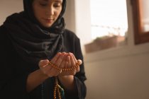 Primer plano de la mujer musulmana con cuentas de oración rezando en casa - foto de stock