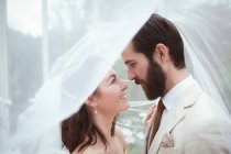 Noiva sorridente e noivo em pé sob o véu — Fotografia de Stock