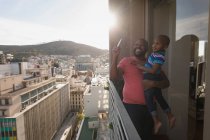 Père portant son fils et prenant des photos avec smartphone dans le balcon à la maison . — Photo de stock