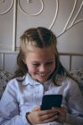 Счастливая девочка с мобильным телефоном на кровати дома — стоковое фото