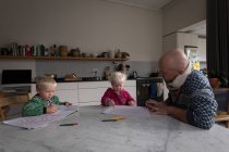Père aidant les enfants à dessiner à table dans la cuisine à la maison . — Photo de stock