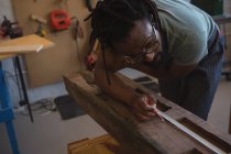 Carpintero midiendo tablón de madera con cinta métrica en taller - foto de stock