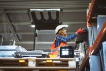 Arbeiterin entlädt Maschinenteil aus Regal in Fabrik — Stockfoto