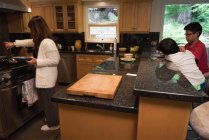 Kinder nutzen digitales Tablet, während Mutter zu Hause in der Küche Essen zubereitet — Stockfoto