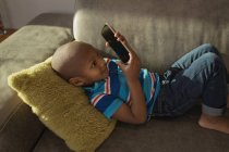 Niño jugando con el teléfono móvil en el sofá en casa . - foto de stock