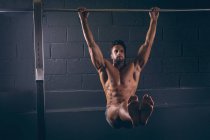 Muscular man exercising on pull-up bar in the fitness studio — Stock Photo