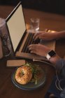 Seção média de mulher usando laptop enquanto tendo hambúrguer no café — Fotografia de Stock