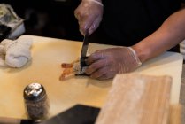 Koch schneidet Sushi-Rolle auf Schneidebrett — Stockfoto