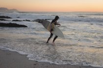 Surfista corriendo con tabla de surf en el mar al atardecer - foto de stock