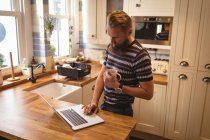 Uomo che prende un caffè mentre usa un computer portatile a casa — Foto stock