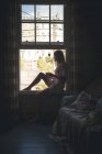Mulher sentada perto da janela enquanto toma café em casa . — Fotografia de Stock