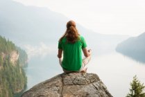 Fit man sitting in meditating posture on the edge of a rock at the time of dawn — Stock Photo
